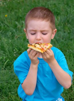 Picnic on the grass. boy   have a dinner with pizza on the meadow .