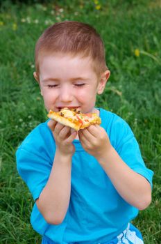 Picnic on the grass. boy   have a dinner with pizza on the meadow .