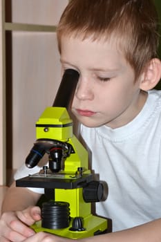 The boy looks in a microscope