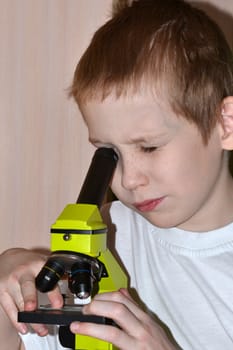 The teenager conducts researches, looking in a microscope