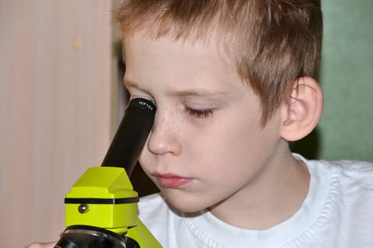 The teenager conducts researches, looking in a microscope