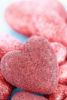 Sparkly red hearts over a blue background. Extreme shallow depth of field with selective focus on large heart in foreground.