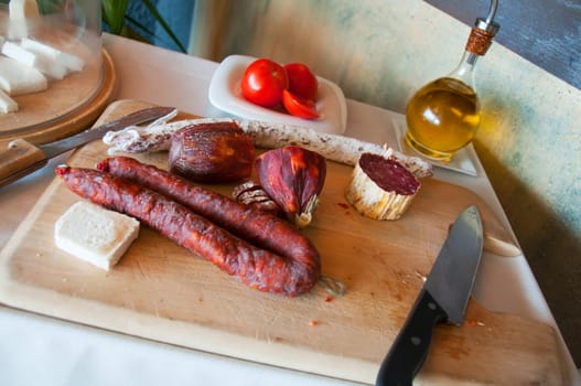 Sausages on a cutting board with knife, olive oil and tomatoes