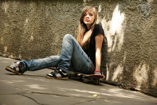 The girl with skateboard sitting against awall