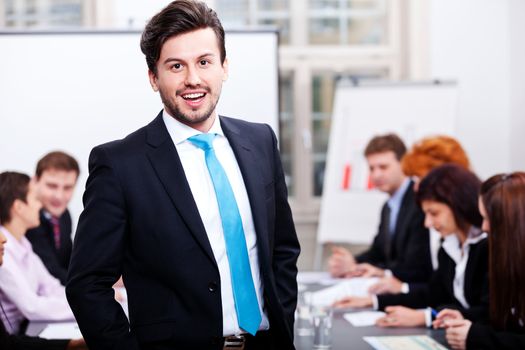 successful business smiling man portrait at office with team in background