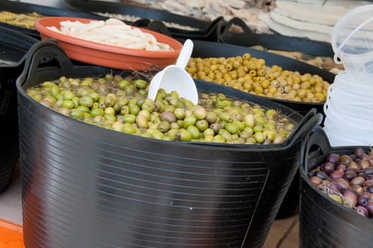 Different sorts of olives in big black barrels