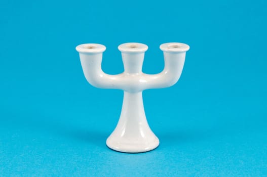 old retro ceramic white candlestick with three places for candle covered with dus on blue background.