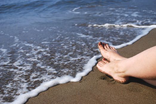 View at the Sea Waves on Shore with Female Legs (Feet) Lying on Sand Beach