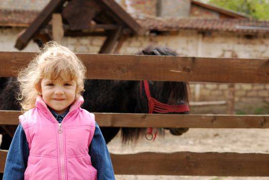 Little girl on the farm with pony horse behind