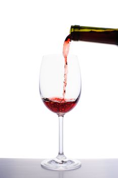 Red wine pouring into wine glass isolated on white background