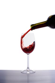 Red wine pouring into wine glass isolated on white background