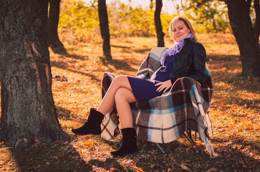 Young pregnant woman sitting on armchair in autumn forest