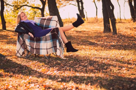 Young pregnant woman sitting on armchair in autumn forest