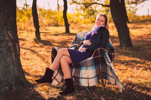 Young pregnant woman sitting on armchair in autumn forest