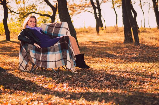 Young pregnant woman sitting on armchair in autumn forest