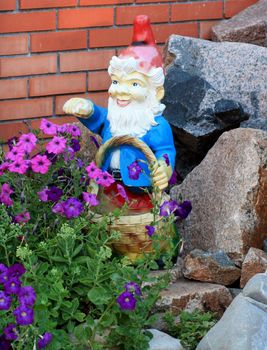 Garden gnome with a basket of flowers and stones against a brick wall