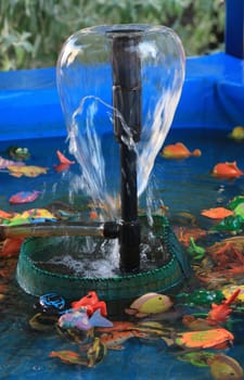Garden fountain in a blue swimming pool with children's plastic fish