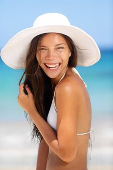Beach woman smiling laughing playful and cheerful in summer sun. Beautiful multiracial Asian Chinese / Caucasian woman wearing white beach hat and bikini.