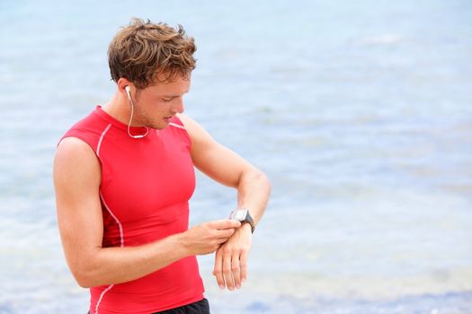 Athlete runner looking at heart rate monitor watch. Man running on beach taking a break in compression t-shirt top.