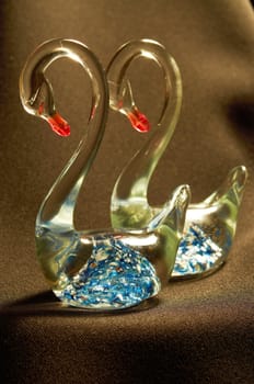 A pair of transparent glass figurines of swans on a black background