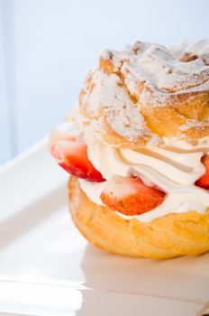 fresh cream puff with whipped cream and strawberries on white plate and light blue wood table