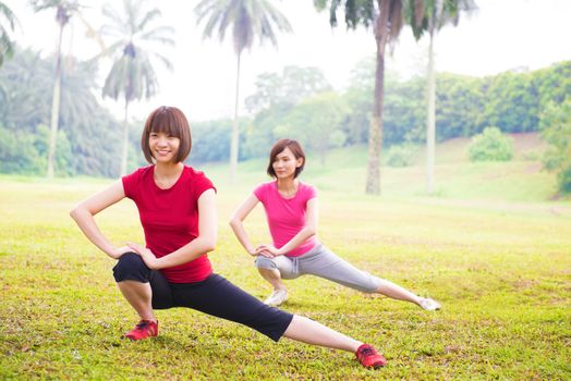 Two cheerful Asian girls stretching outdoor green park