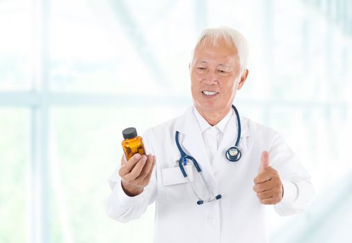 Asian senior doctor holding a bottle of pills, thumb up isolated white background