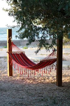 Patterned canvas hammock with tassels between wooden beams under the sea buckthorn on the beach by the sea