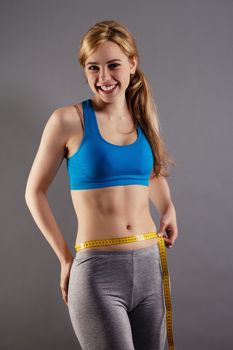 happy fitness woman measuring her waist on gray background