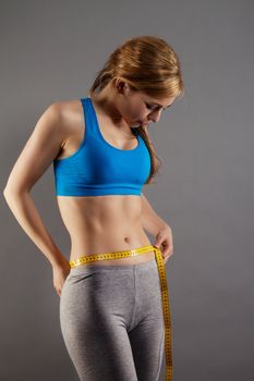 blonde fitness woman measuring her waist on gray background