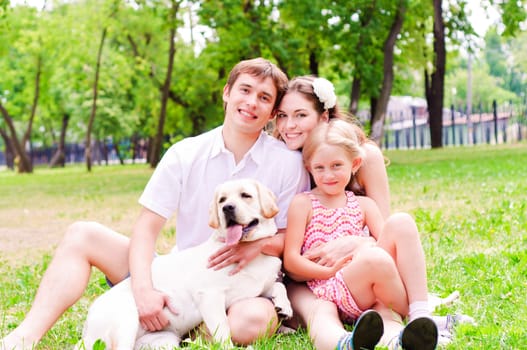 Happy young family with Labrador is resting in the park