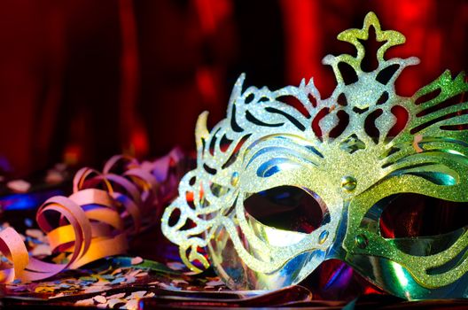 Carnival mask with a red silky background and confetis and streams on the table.