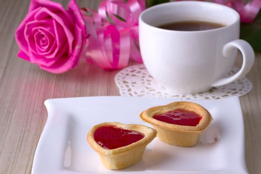 Holiday Tartlets with jam near the cup of tea on the background of roses