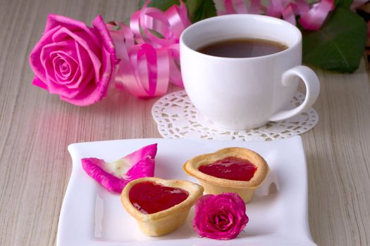 Holiday Tartlets with jam near the cup of tea on the background of roses