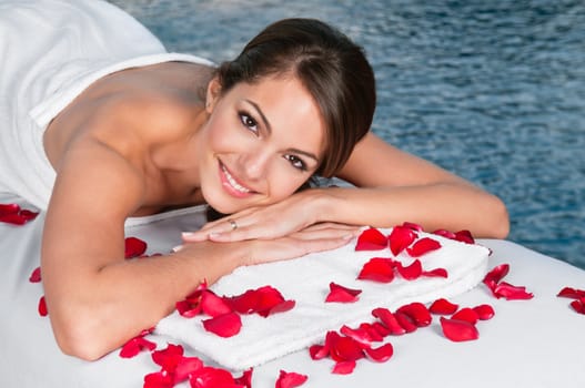 Portrait of beautiful young female lying on massage bed with rose petals in foreground