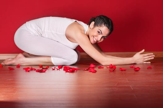 Portrait of a cute young woman doing yoga in a child pose near rose petals