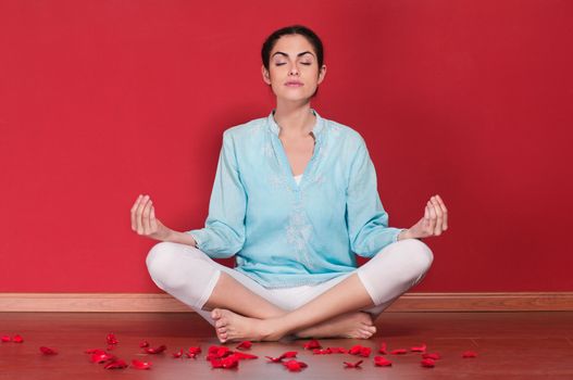 Young woman practicing yoga in the lotus position against colored background