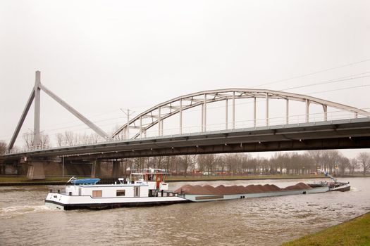 ship in canal transporting sand under bridge in The Netherlands