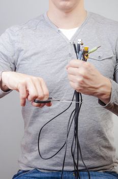 An image of man holding many cables with plug and scissors in other hand