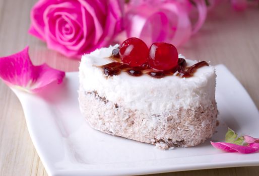 Celebratory cake with cherries on a background of pink roses