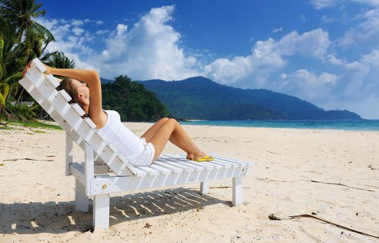 Girl on a tropical beach sitting at chaise lounge