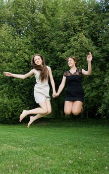 Two young cheerful women jumping and laughing at summer green park.