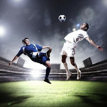 two football players in jump to strike the ball at the stadium