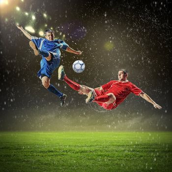 two football players in jump to strike the ball at the stadium