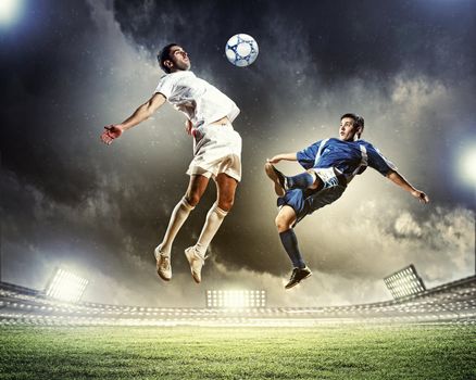 two football players in jump to strike the ball at the stadium
