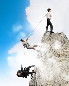 Image of three businesspeople pulling rope atop of mountain