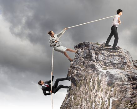 Image of three businesspeople pulling rope atop of mountain