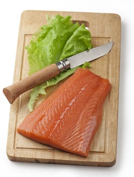 Chunk of raw salmon's fillet with knife and lettuce on the wooden board