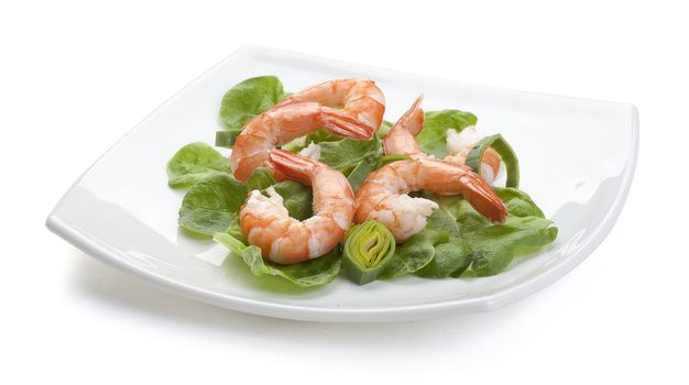 Some shrimp's tails with fresh leek and lettuce on the white plate