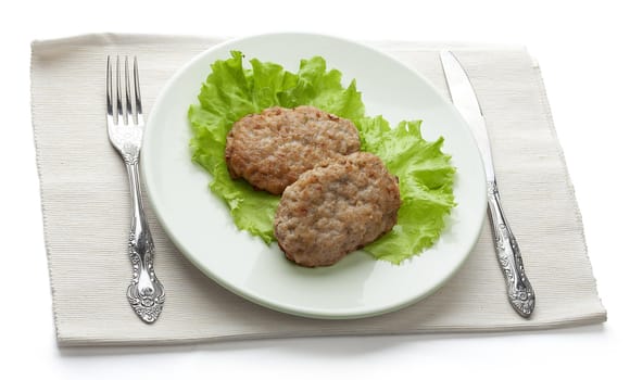 White plate with two rissoles and lettuce on the napkin with fork and knife